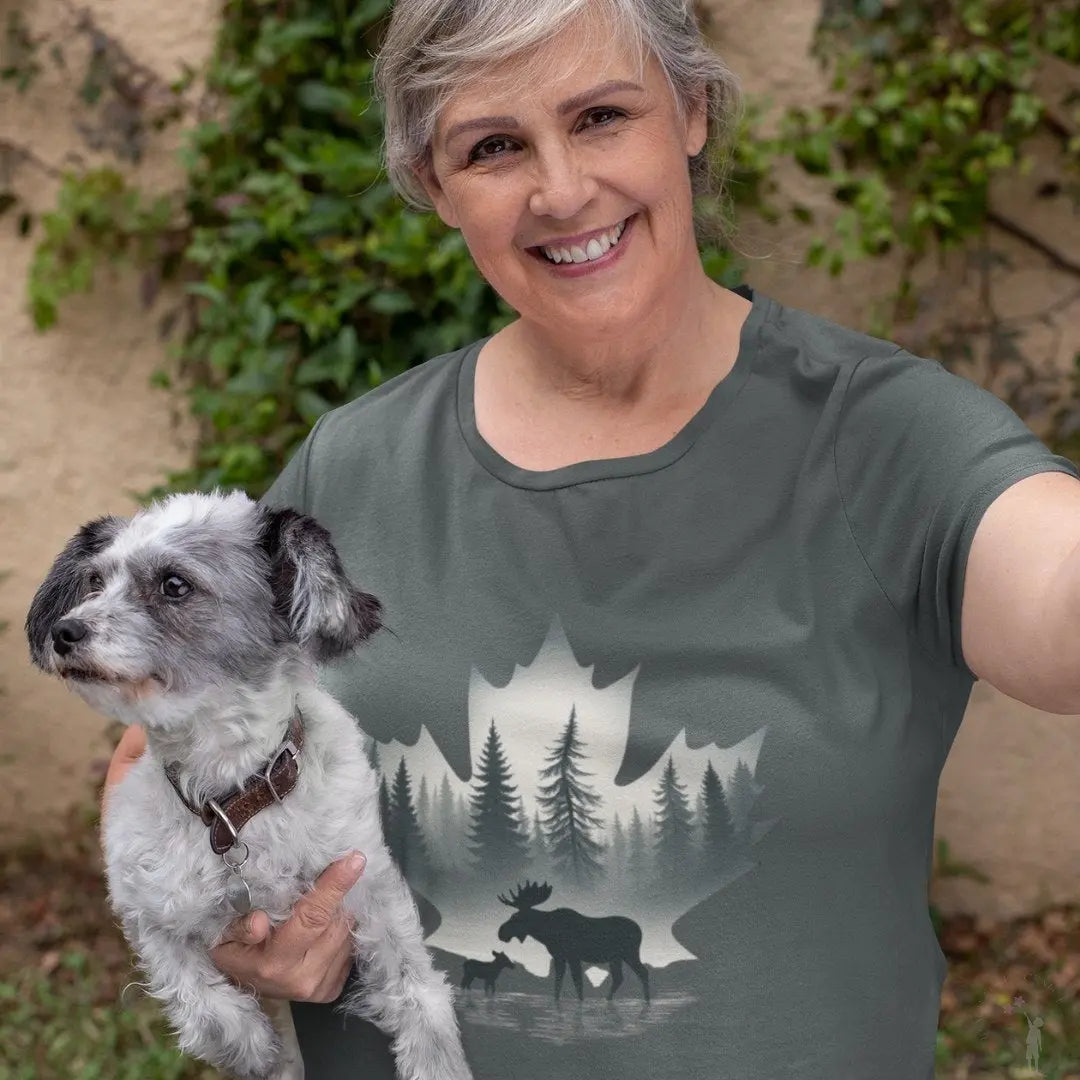 Woman holding a dog wearing a t-shirt with a moose and forest design.