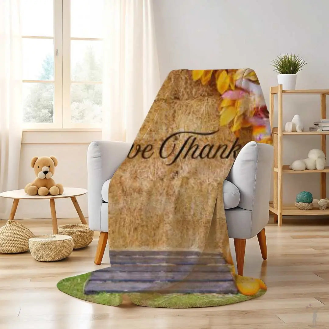 Floral-themed blanket with 'Be Thankful' text draped over a chair in a cozy living room.